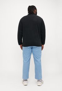 Black long-sleeve top with a relaxed fit, paired with light blue straight-leg jeans and grey sneakers. Textured fabric visible on top.