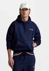 Navy blue hoodie made of cotton blend, featuring a front pocket, drawstring hood, and white "POLO SPORT" logo on the chest.