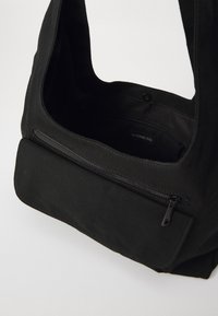 Sort tote taske med en bred, åben top, der har en frontlomme med lynlås og glat tekstur; lavet af holdbart stof med et enkelt design.