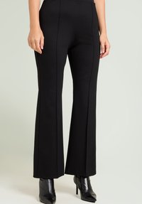 Zwarte wijde broek gemaakt van rekbaar materiaal, met frontnaad en een gladde textuur, gecombineerd met zwarte laarzen met hoge hakken.