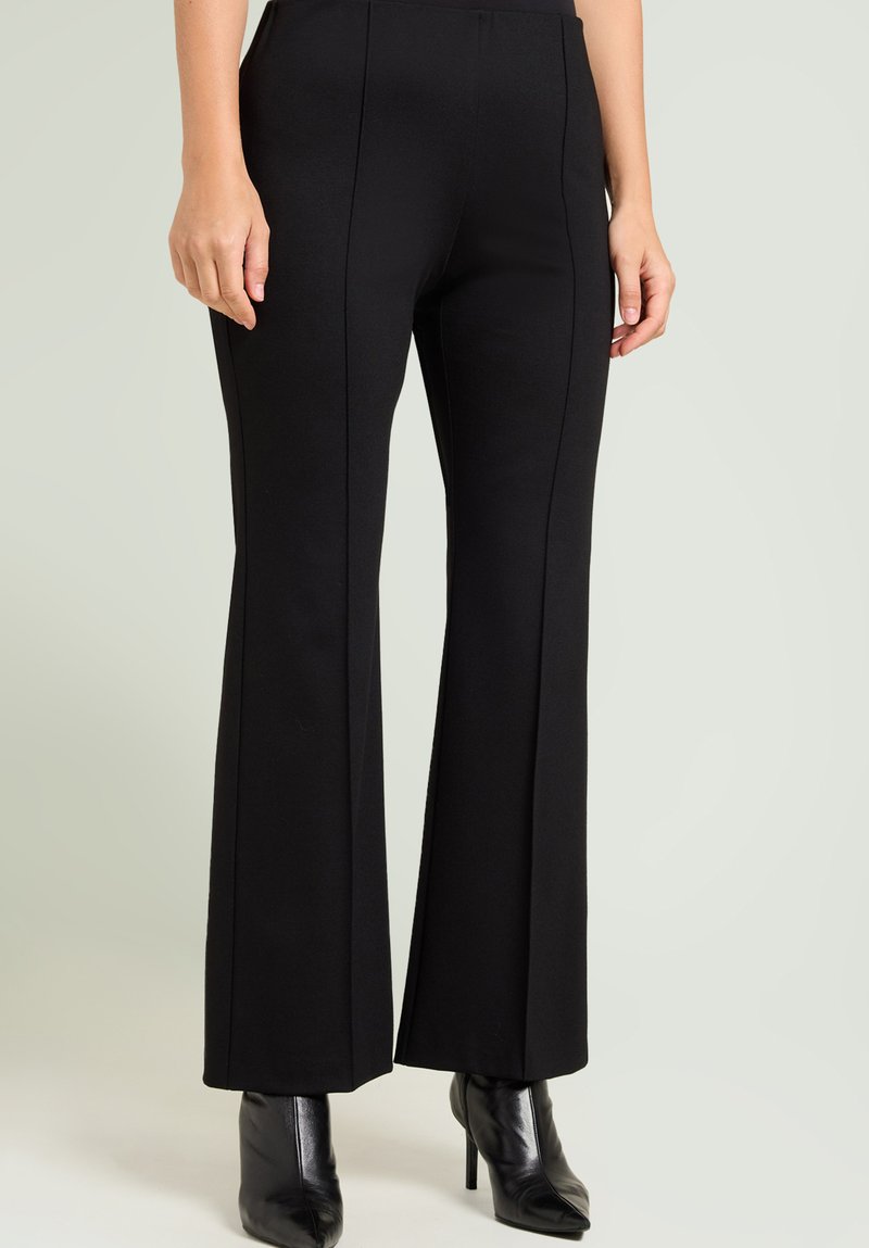 Zwarte wijde broek gemaakt van rekbaar materiaal, met frontnaad en een gladde textuur, gecombineerd met zwarte laarzen met hoge hakken.