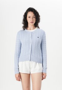 Light blue knitted cardigan with a textured cable pattern, ribbed cuffs, and a round neckline. Features a small heart logo on the left side.
