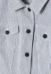 Koszulka w paski w granatowo-białe linie, z dwoma przednimi kieszeniami, czarnymi guzikami i klasycznym kołnierzykiem. Tekstura z bawełny.