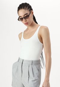 White scoop-neck tank top made of cotton, paired with tailored gray high-waisted shorts with pleats, featuring sleek black sunglasses.