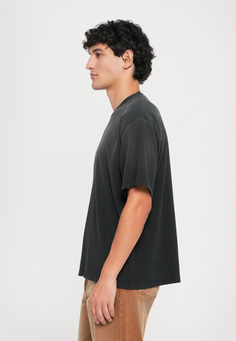 Black cotton t-shirt with short sleeves and a rounded neckline, featuring a relaxed fit and visible stitching details.