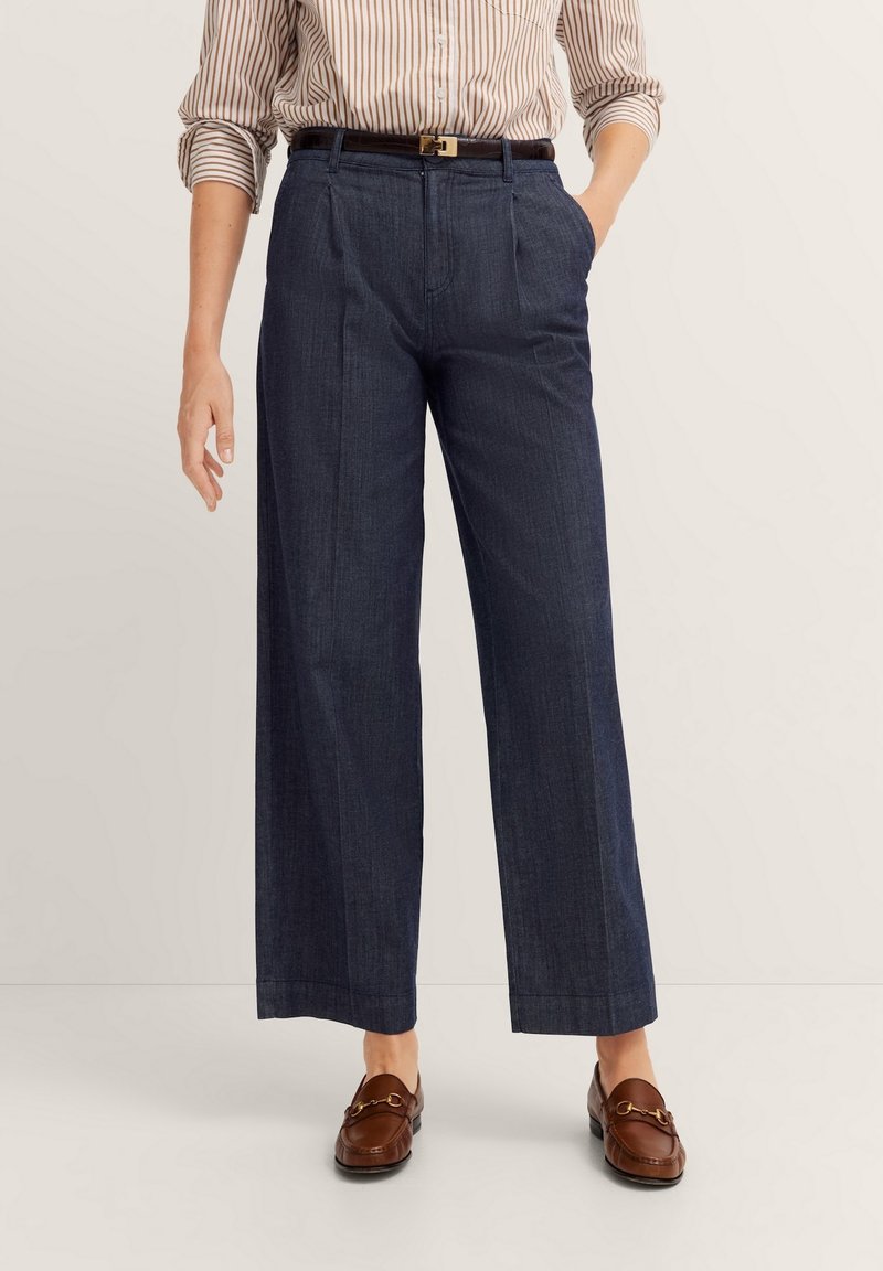 Marineblaue weit geschnittene Hose aus strukturiertem Stoff, mit einer definierten Taille, Falten und Seitentaschen, kombiniert mit braunen Mokassins.