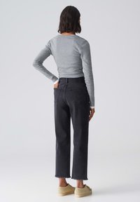 Top gris de manga larga combinado con jeans de mezclilla negros de cintura alta, con un dobladillo deshilachado y un corte relajado. El modelo lleva zapatos de color claro.