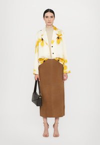 Lightweight cream jacket with yellow floral print, paired with a brown knee-length skirt. Model holds a black bag, wearing strappy nude heels.