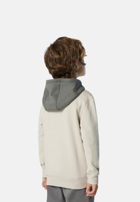 Sudadera de color beige claro con capucha gris. Presenta puños y dobladillo acanalados, textura suave y un corte relajado. La vista posterior muestra detalles de costura.