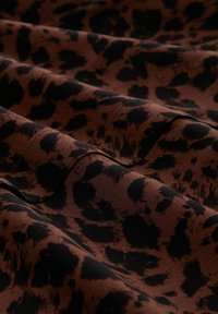 Brown fabric with irregular black leopard spots, shown in soft folds with visible texture and stitching.