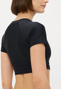 Μαύρο κομμένο τοπ με κοντά μανίκια, λεία υφή και εφαρμοστή σχεδίαση. Διαθέτει μια μικρή μωβ λεπτομέρεια στο πλάι.