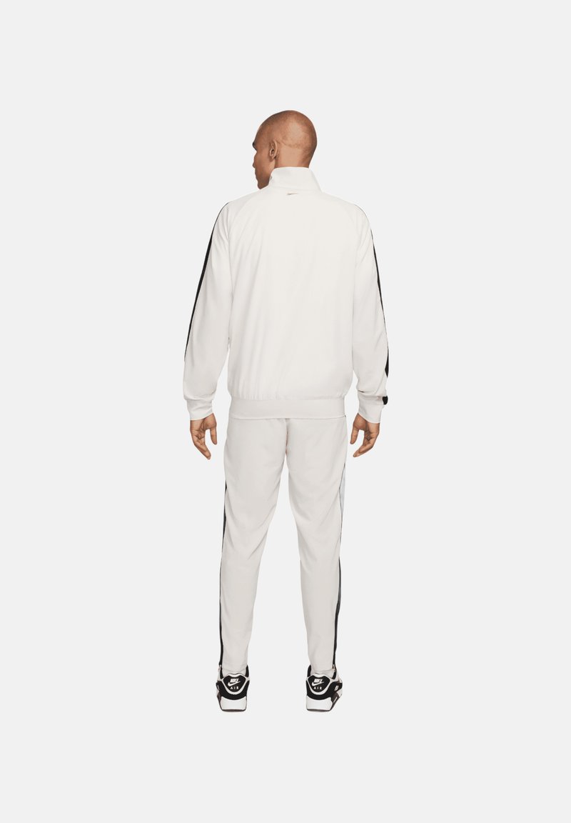 Chándal blanco que incluye una chaqueta con cremallera y franjas laterales negras, junto con pantalones a juego. Fabricado con tejido suave y diseñado con puños elásticos.