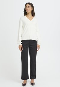 Pull blanc à col en V avec manches longues, associé à un pantalon noir à jambes larges et des chaussures à bout pointu de couleur sombre. Textures simples et lisses.