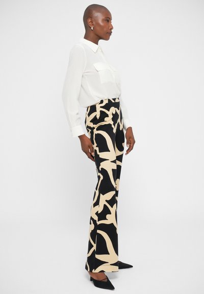 Zwart en beige gestreepte broek met uitlopende pijpen, gecombineerd met een witte blouse met knopen en zwarte puntige hakken. Gladde stoftextuur.