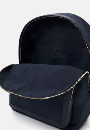 Donkerblauwe rugzak met open bovenklep, gouden rits en binnenvak, die minimalistisch ontwerp en gladde stof toont.