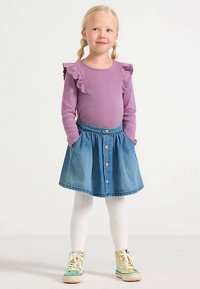 Top a maniche lunghe lilla chiaro con volant, gonna a trapezio in denim, collant bianchi e sneakers multicolori con design con lacci.