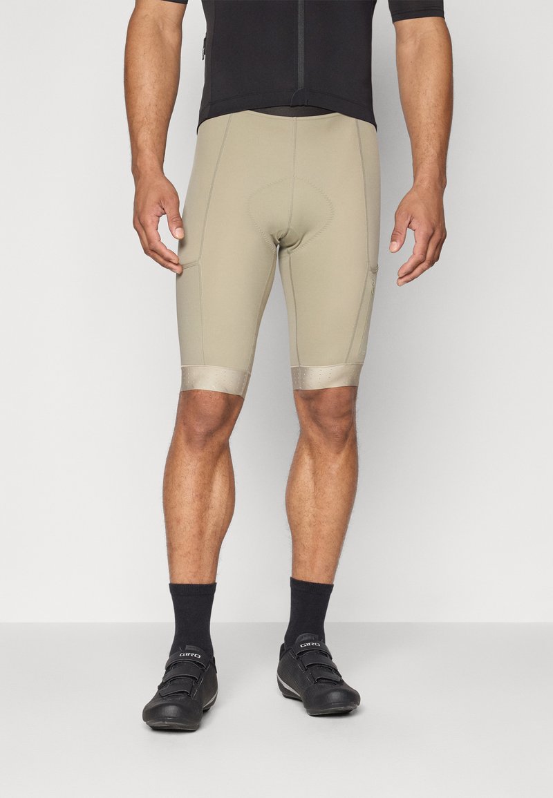Pantaloni corti da ciclismo beige con inserto imbottito, caratterizzati da una vestibilità aderente e dettagli riflettenti, abbinati a scarpe e calze da ciclismo nere.