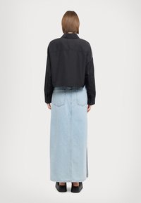 Jachetă neagră scurtă cu guler, asortată cu o fustă maxi din denim albastru deschis, cu o fanta și buzunare la spate. Pantofi negri completează ținuta.