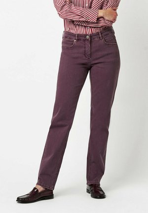 Lila gerade geschnittene Jeans mit Gürtelschlaufen, fünf Taschen und dezenten Stickdetails, kombiniert mit dunklen Slippern und einem gestreiften Hemd.