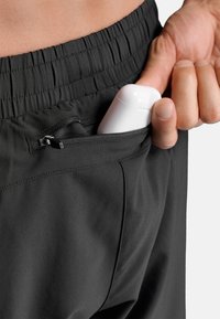 Zwarte sportshorts met een gerimpelde tailleband, voorzien van een ritssluiting waarin een wit hoesje zit. Gladde stoftextuur, minimalistisch ontwerp.