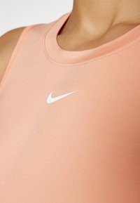 Persikofärgad Nike-linne med rund halsringning, slät textur och en liten vit Nike-logga på framsidan.