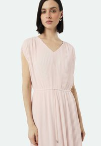 Plissiertes, hellrosa Kleid mit V-Ausschnitt und kurzen Ärmeln; verfügt über eine Kordelzug taille und eine fließende Silhouette. Glatte Stofftextur.