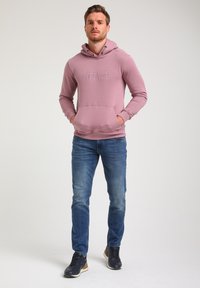 Lys rosa hoodie med en frontlomme og logo print, parret med blå jeans og sorte sneakers, med en slank pasform og blød tekstur.
