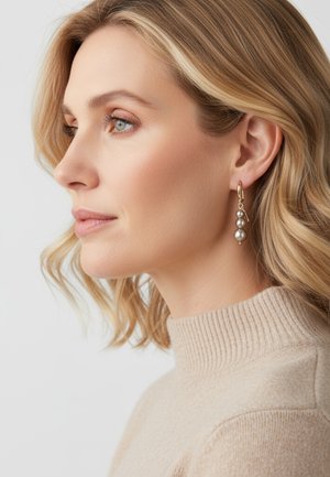 Gold hoop earrings with three hanging gray pearls, set against a beige ribbed sweater. Hair styled in soft waves.