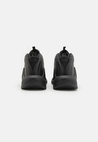 Chaussures de sport noires avec un dessus de chaussure texturé, un talon renforcé et un col rembourré. Comprend un détail de logo à l'arrière et une semelle flexible.