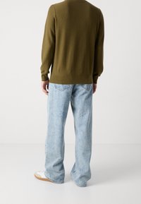 Pull en laine texturé vert avec des manches longues, associé à un jean bleu clair à jambes larges et des baskets blanches avec des semelles brunes.