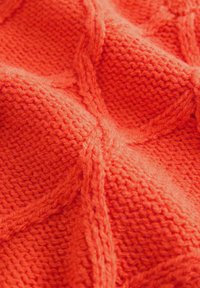 Strickdecke in einem leuchtenden Orange, mit einem strukturierten Muster aus erhöhten, sich kreuzenden Linien und einem weichen, flauschigen Gefühl.