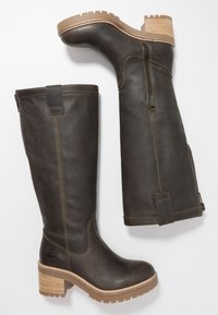 Hnědé kožené kozačky sahající ke kolenům s texturovaným povrchem, bočním zipem a naskládaným dřevěným podpatkem. Drážkovaná gumová podrážka pro lepší trakci.