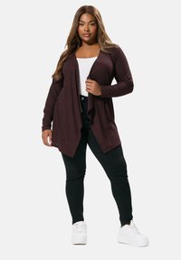 Mörkröd öppen cardigan med ribbad textur, långa ärmar och en fallande design, kombinerad med svarta byxor och vita sneakers.