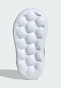 Suela de zapatilla blanca con texturas en forma de burbuja redondeada y estrías, con un logo "adidas" en relieve en el centro.