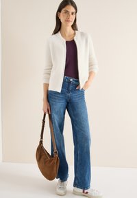Biały, puszysty kardigan, fioletowy top, niebieskie jeansy o szerokich nogawkach i białe tenisówki z czerwonymi akcentami. Brązowa zamszowa torba na ramię. Gładkie faktury.