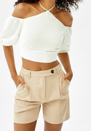 Witte off-shoulder cropped top met pofmouwen, gecombineerd met beige op maat gemaakte short met knoop en plooien. Soepele stoftextuur.