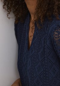 Marinblå texturerad topp med en spetsdesign i geometriska mönster och en V-ringning. Korta ärmar framhäver det intrikata tyget.