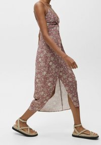 Langes, ärmelloses Kleid in Mauve mit floralem Druck und einem gedrehten Vorderdesign. Verfügt über einen seitlichen Schlitz und schwingt sanft bis zur Mitte der Wade. Kombiniert mit Sandalen.