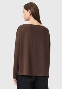 Top marrone a maniche lunghe con una vestibilità ampia e un collo largo, realizzato in tessuto morbido e liscio. Caratterizzato da un orlo dritto e spalle scese.