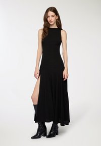 Abito maxi nero senza maniche con un corpino attillato e una gonna ampia e fluida, caratterizzata da un alto spacco laterale. Abbinato a stivali neri lucidi al ginocchio.