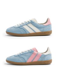 Deux baskets en daim bleu clair avec des semelles marron, l'une avec des bandes blanches et un talon rose, l'autre avec des bandes roses et un talon blanc.