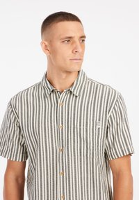 Camisa de manga corta con rayas verticales en blanco y negro, con un cierre de botones en el frente, un bolsillo en el pecho y botones de madera.