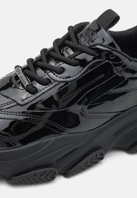 Sorte patent lær sneakers med teksturerte detaljer, tykk svart såle og flate svarte lisser. Har merking på tungen og siden.
