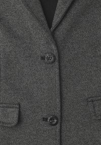 Szary, teksturowany blezer z klapami z wyłaniaczami, dwoma kieszeniami z przodu i dwoma czarnymi guzikami. Tkanina ma subtelny wzór plecionki.