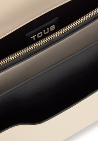 Interior de bolsa en beige y negro con una cremallera en tono dorado y una etiqueta negra que muestra el nombre de la marca "TOUS."