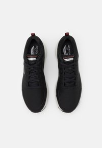 Chaussures de sport noires avec dessus en maille texturée, fermeture à lacets et semelle blanche rembourrée. Présente le logo "Skechers Arch Fit".