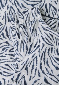 Weißer Stoff mit einem navyblauen Tierdruckmuster, das gezackte Linien aufweist. Die Textur erscheint glatt mit einem leichten Glanz.