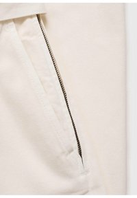 Tissu en coton blanc avec une poche zippée diagonale à dents de zip foncées, surface texturée et lignes modernes et épurées.