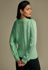 Pull en maille vert menthe avec un design côtelé à rayures verticales, des manches longues et un col rond. Fini texturé sur l'ensemble.