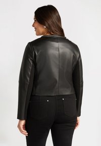 Chaqueta de cuero negra corta con un acabado suave y un detalle de cadena en el collar, combinada con jeans negros que presentan detalles de botones metálicos.